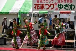 大人の女性と女の子たちがフラダンスの衣装とグリーンレイを頭と首から下げて踊りを踊っている写真