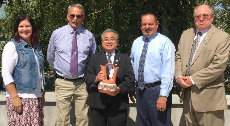 笑顔で壺のような物を持つ田村村長とマグナメトロタウンシップ議員の方々が並んでいる写真