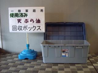 一般家庭用使用済み天ぷら油回収ボックスと書かれてある看板の横に蓋つきのプラスチック製ボックスが置かれてある写真