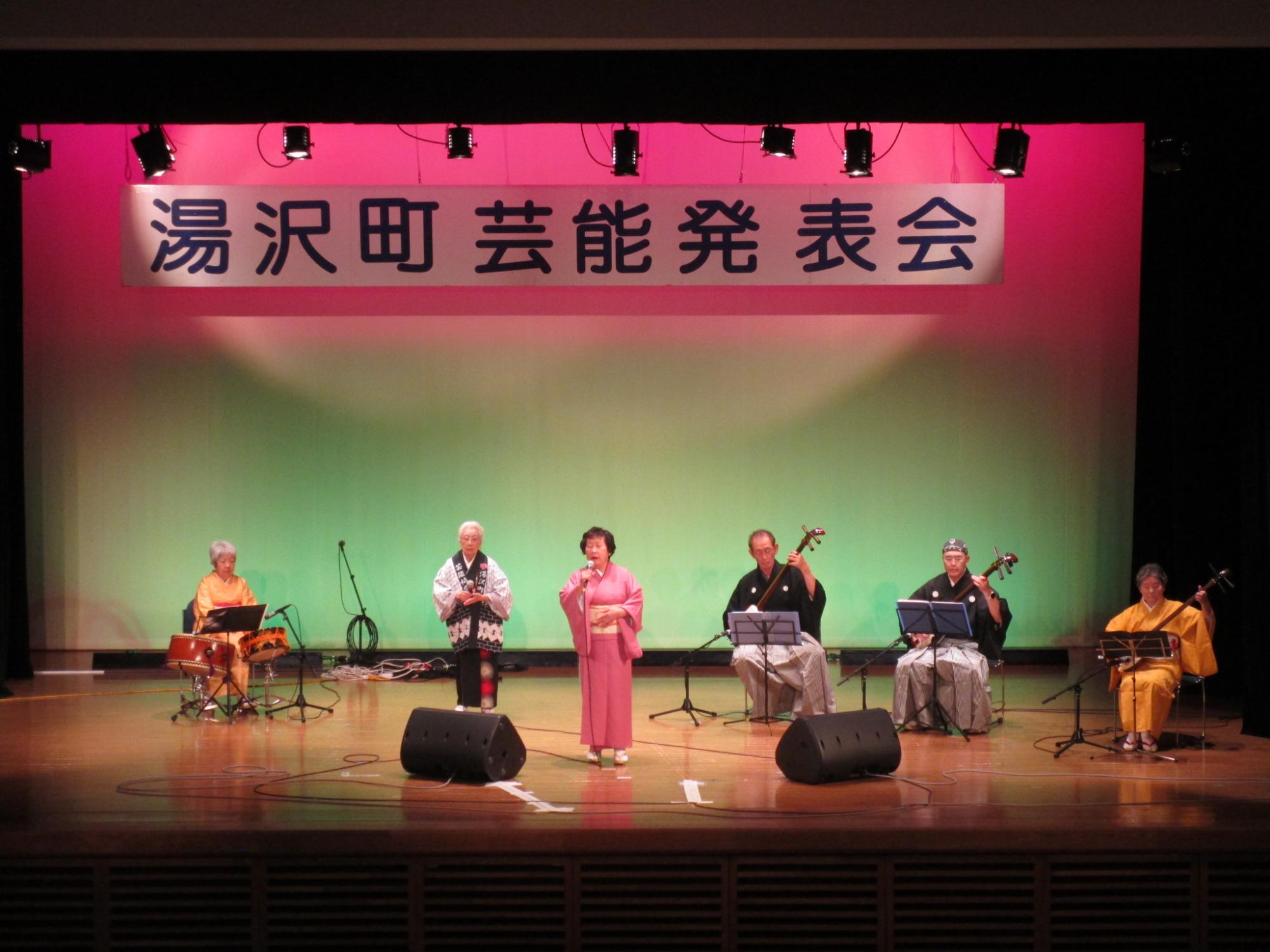 舞台の上で民謡を披露するすみれ会のメンバーの写真