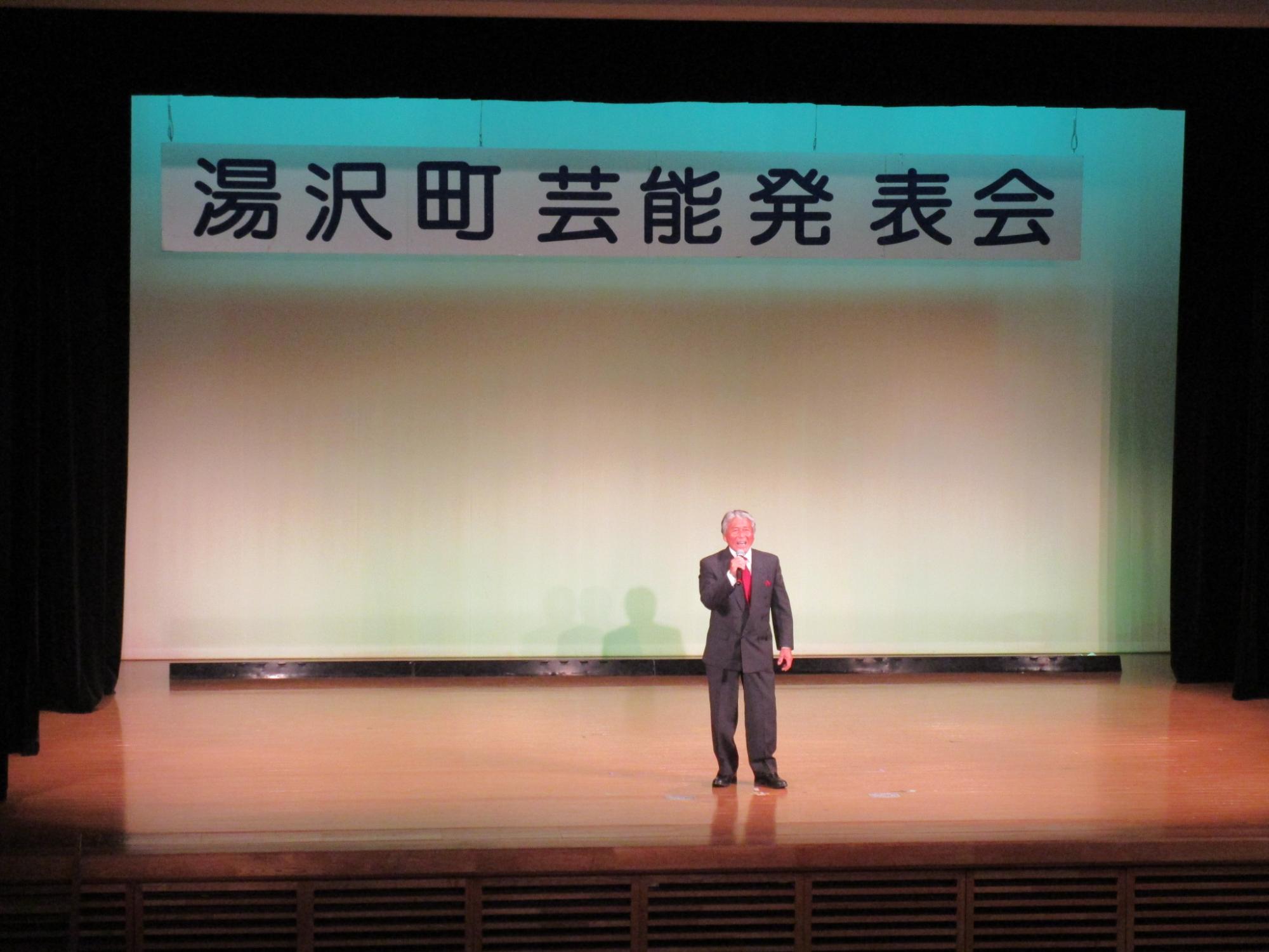 舞台で歌唱する山崎会長の写真
