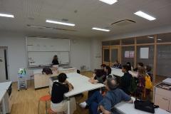 前方の白板に講師の方が板書しており、マグナのみなさんがテーブルの席に着いて授業を受けている日本語学習の様子の写真