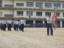 制服を着て、消防旗を持った隊員を先頭に、消防隊員の方々が行進をしている写真
